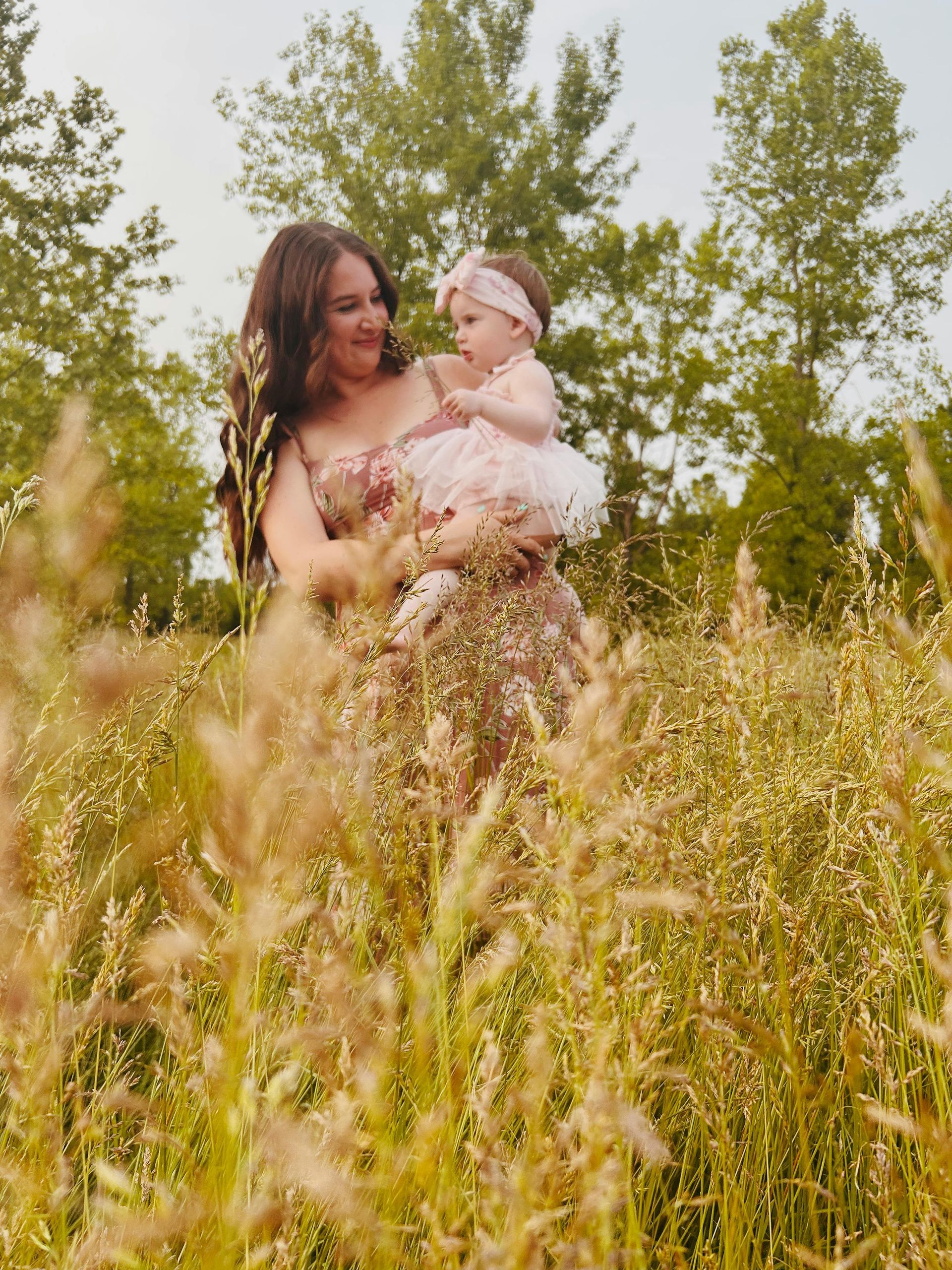 A woman is holding a baby in a field of tall grass.
