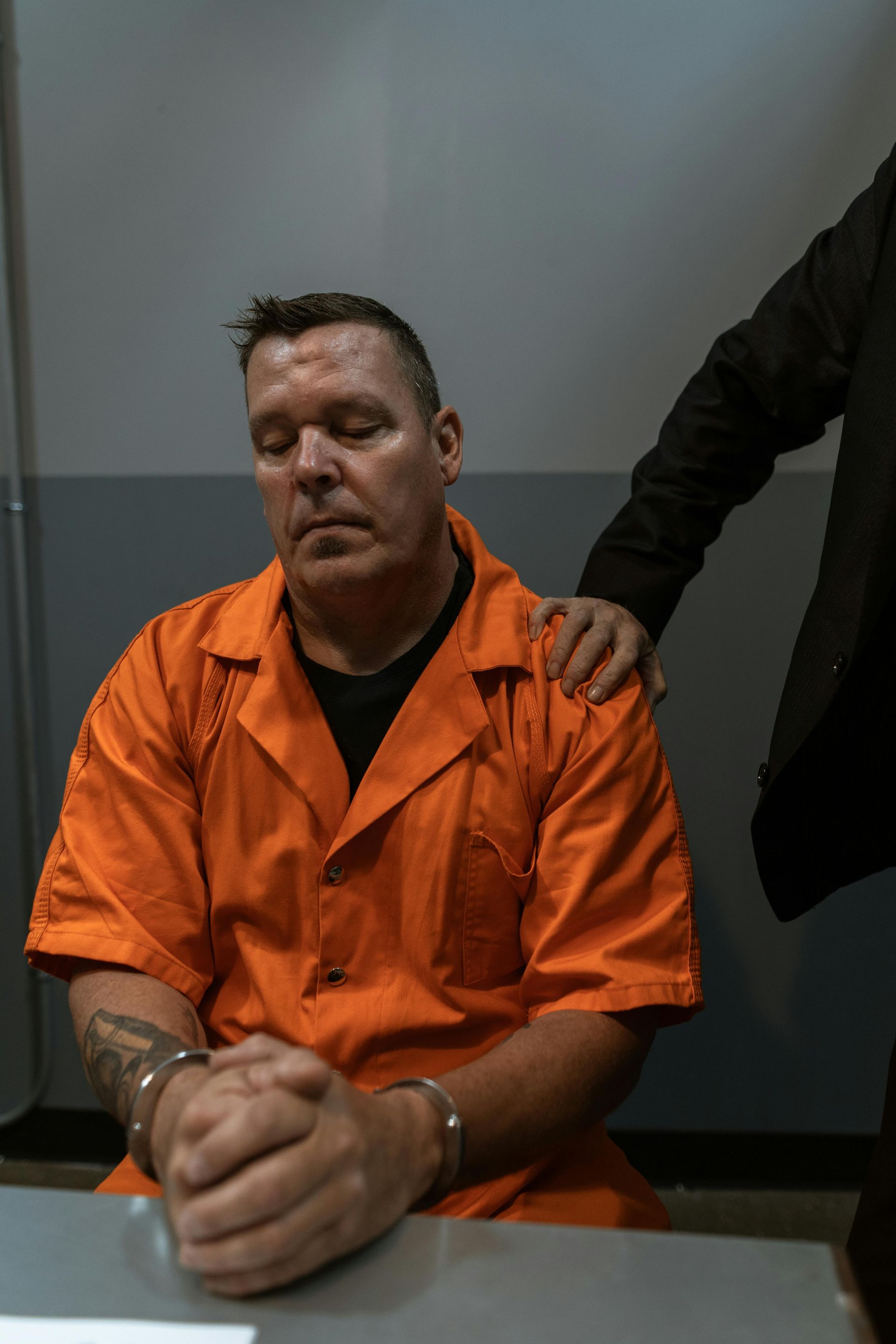 A man in an orange jumpsuit is sitting at a table with his eyes closed.