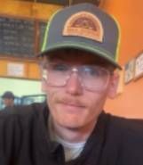 A man wearing glasses and a baseball cap is sitting at a table in a restaurant.