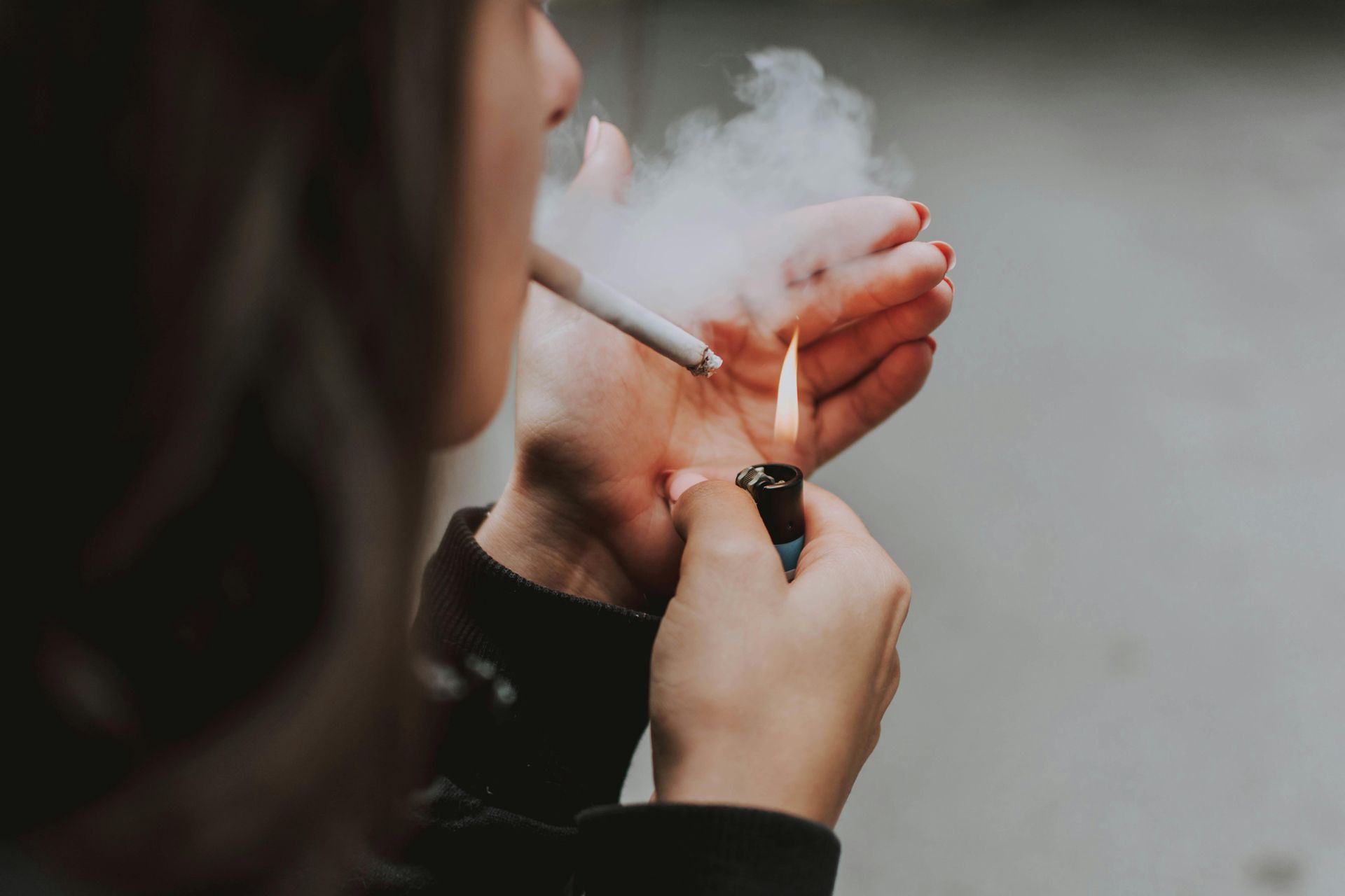 Person lighting a cigarette with a lighter, smoke billowing upward.