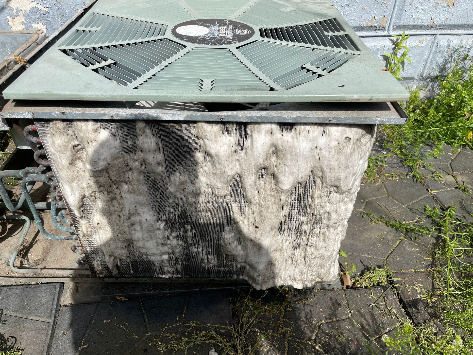 Dirty, old air conditioning unit on brick, covered in dirt and grime, with green top.