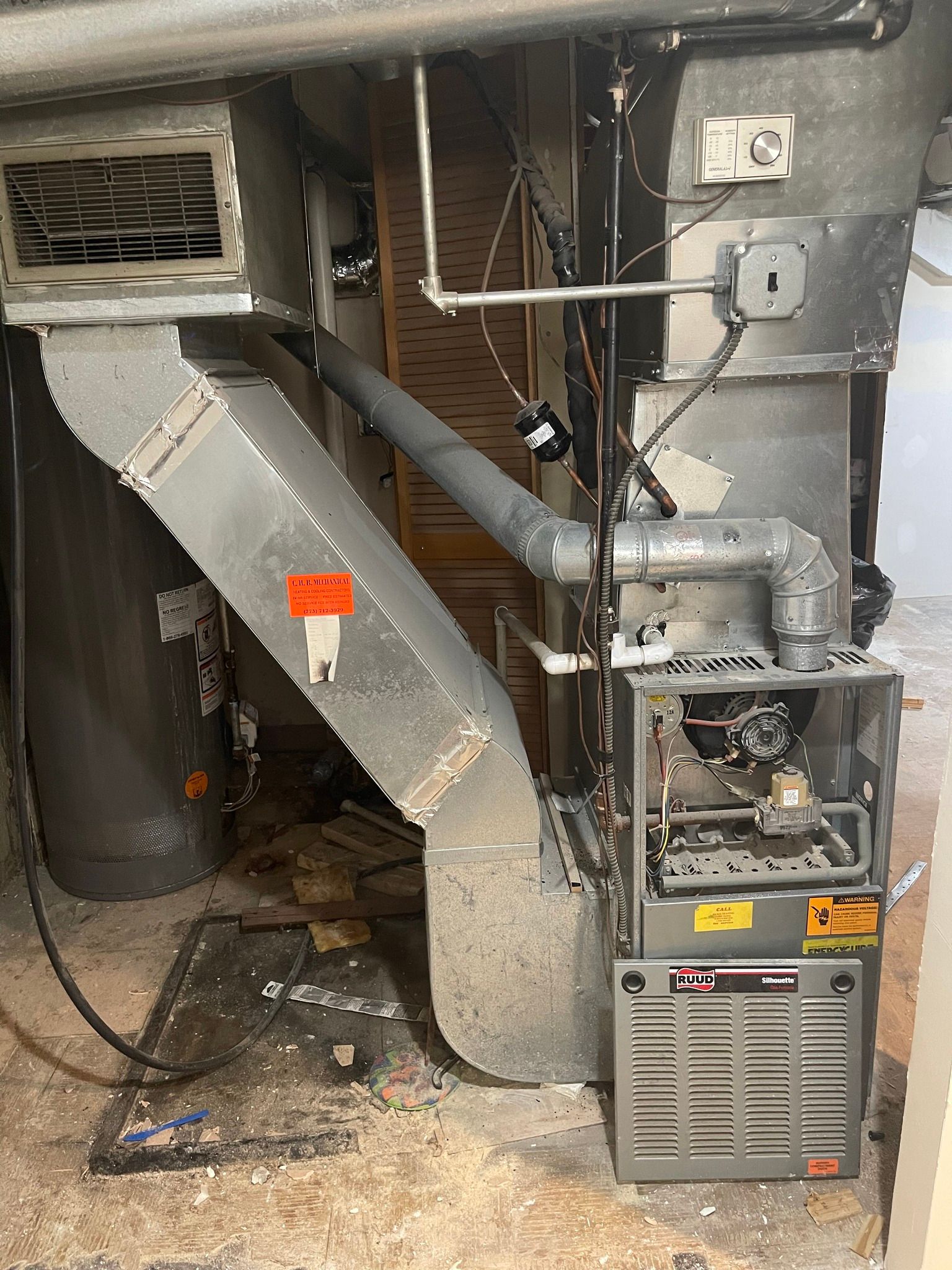 Furnace with ductwork, water heater, and debris in a basement.