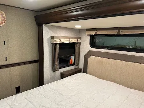 Hotel bedroom with white bed, headboard, and small fireplace beside a dark window.