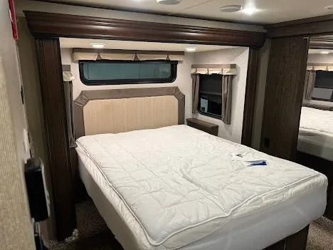 Interior of a cozy RV bedroom with a queen bed, beige headboard, and dark wood trim