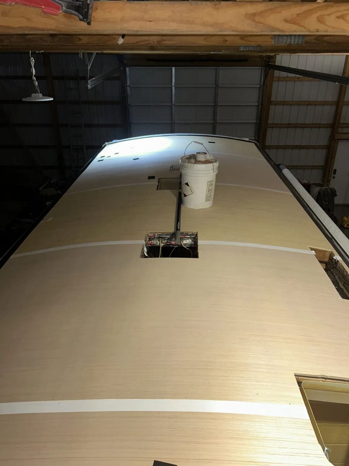 Interior of a trailer roof with white insulation panels and a central vent under wooden framing.