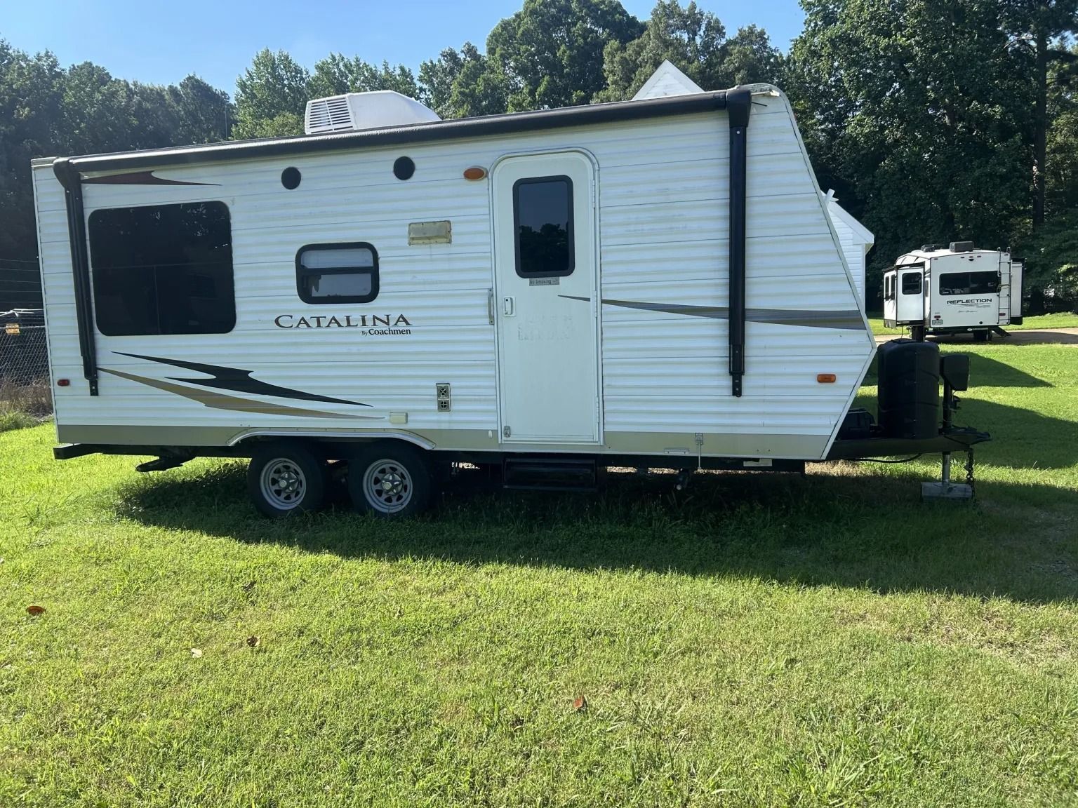 White travel trailer parked on grass under trees on a sunny day