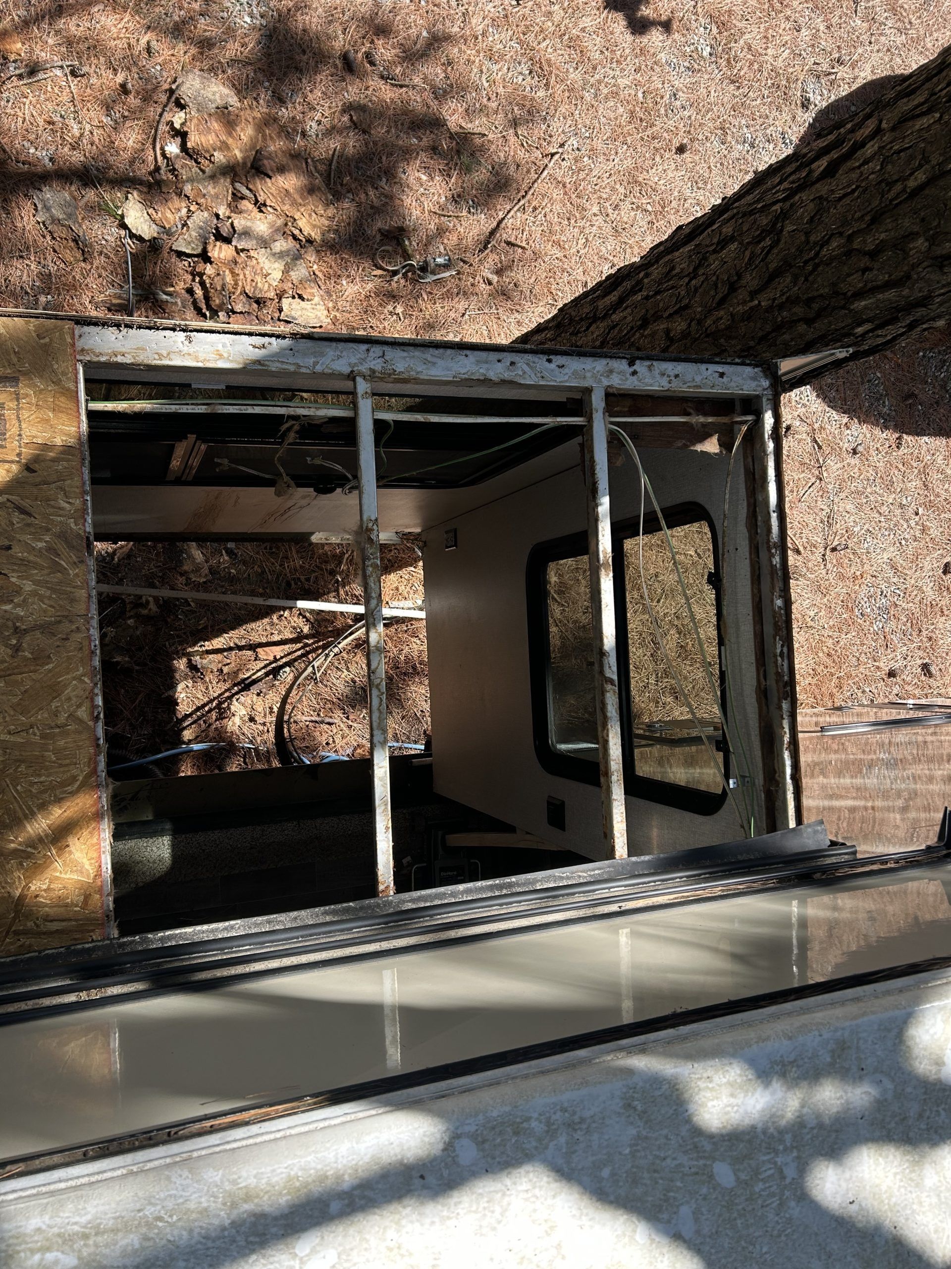 Open, damaged storefront window with glass framing and a view into a dim interior, beside a textured wall and shadows.