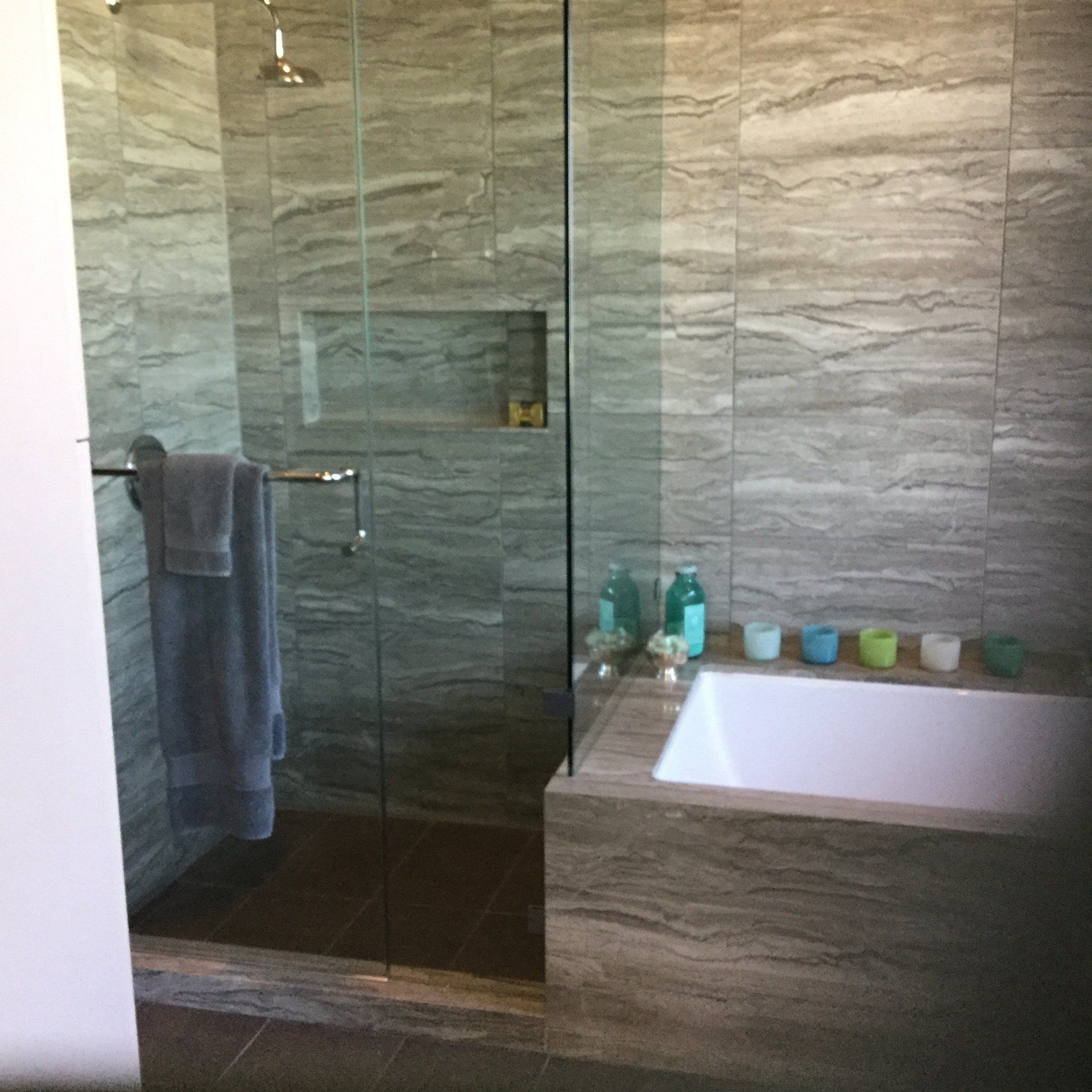 A modern bathroom features a glass-enclosed shower next to a built-in soaking tub, both tiled in a gray, textured stone.