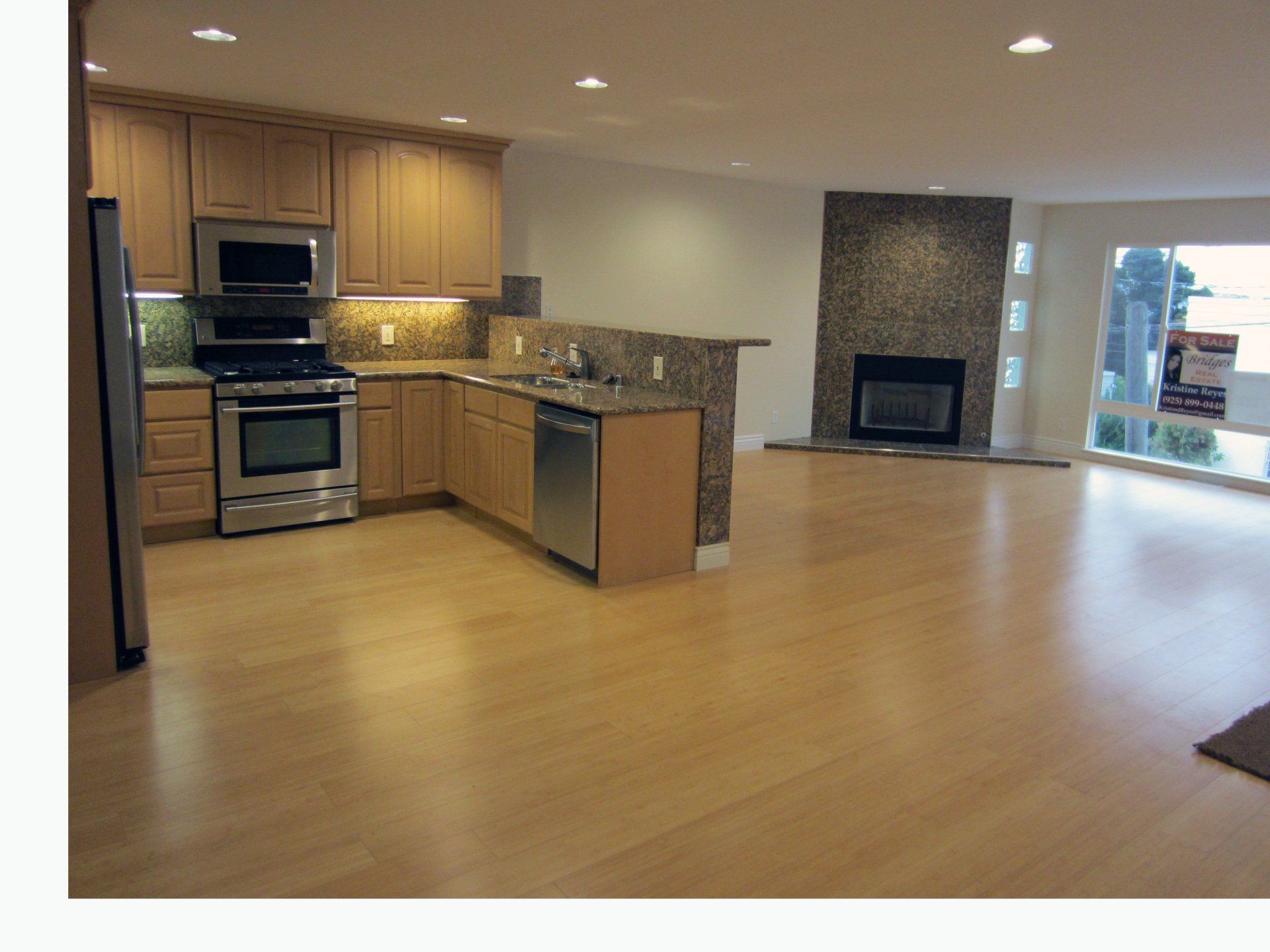 A modern, open-concept kitchen with wood cabinets and stainless appliances, leading to a living area with a stone fireplace.