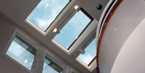 Low-angle view of several rectangular skylights in a ceiling, letting in natural light from a bright, cloudy sky.