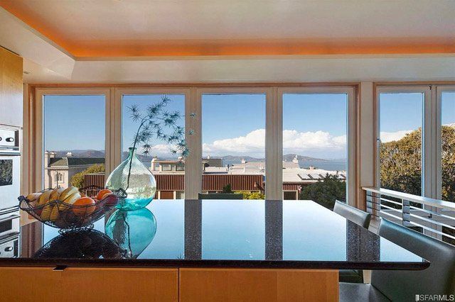 A kitchen island with a dark countertop and a fruit bowl, overlooking a scenic view through large, floor-to-ceiling windows.