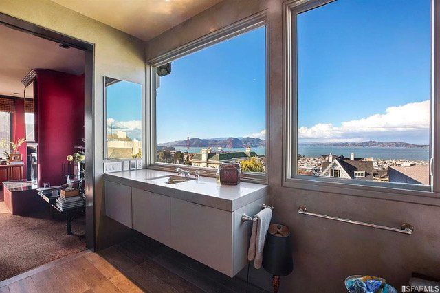 A modern bathroom vanity with a basin sink sits before a large window overlooking a coastal city view.