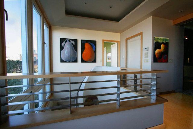A landing area with a modern metal railing, two pear paintings on the wall, and another piece of art on the side.