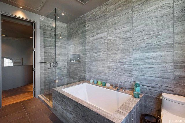 Modern bathroom with grey stone walls, a white soaking tub, and a glass-enclosed shower.