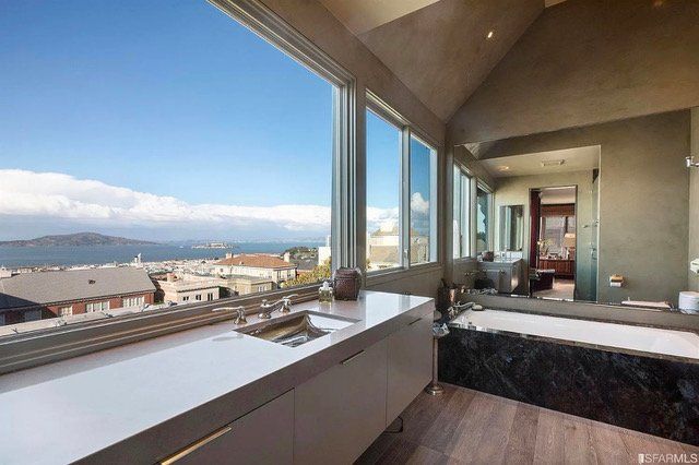 A luxury bathroom with a bathtub, white vanity, and large windows offering a panoramic ocean and city view.