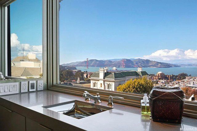 A kitchen sink sits before a wide window overlooking a scenic view of San Francisco and the Golden Gate Bridge.