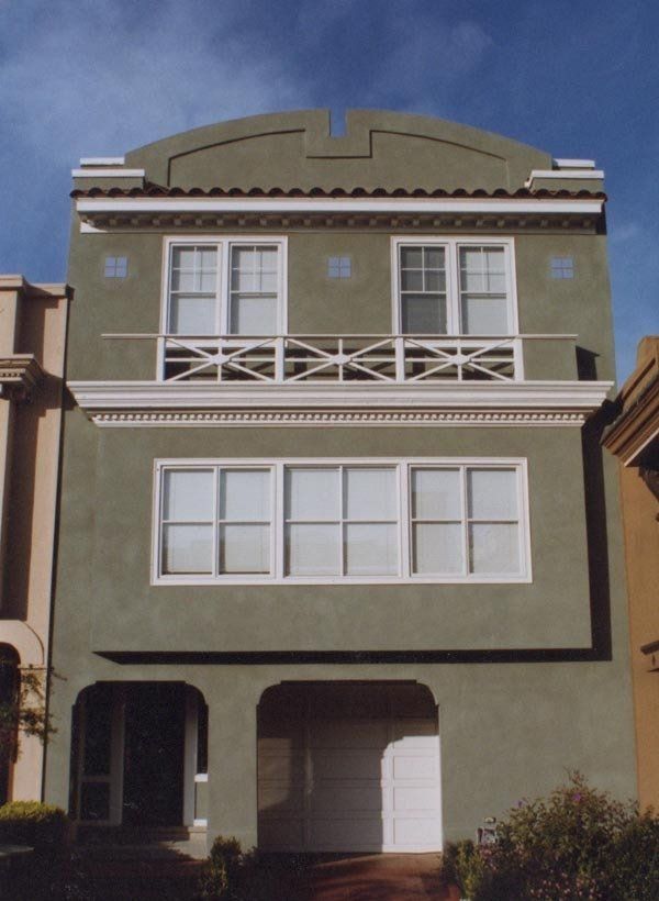 A sage green multi-story residential building featuring a front balcony, white window trim, and a ground-floor garage.
