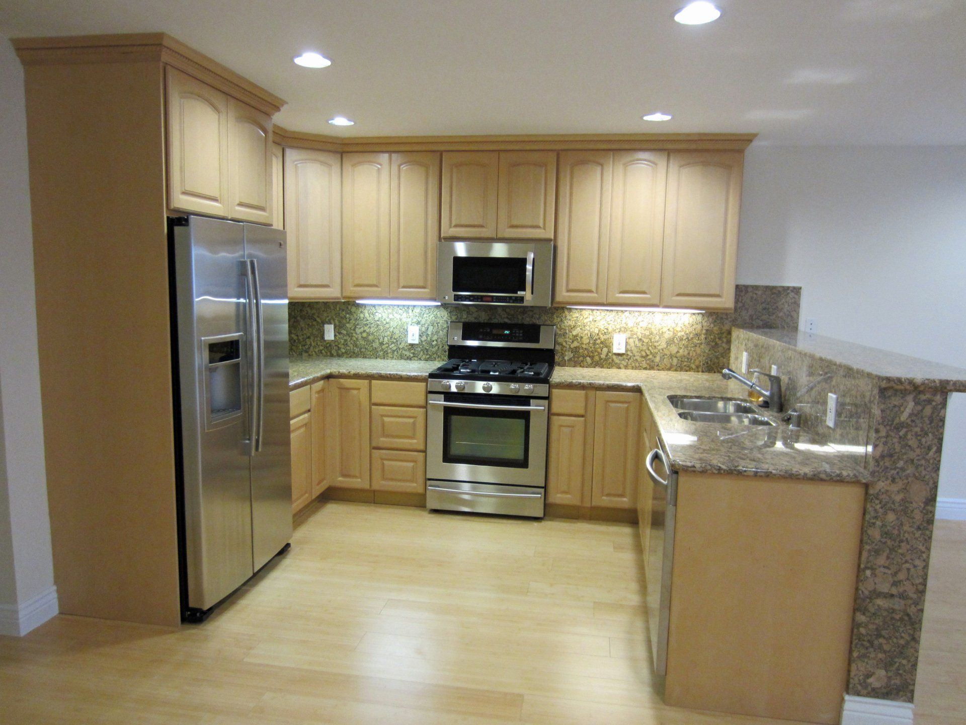 A modern kitchen with light wood cabinets, granite countertops, and stainless steel appliances.