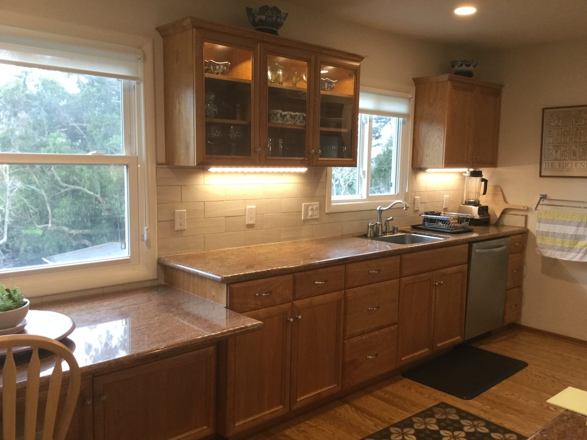 A kitchen with wooden cabinets, granite countertops, a tiled backsplash, and windows looking out onto trees.