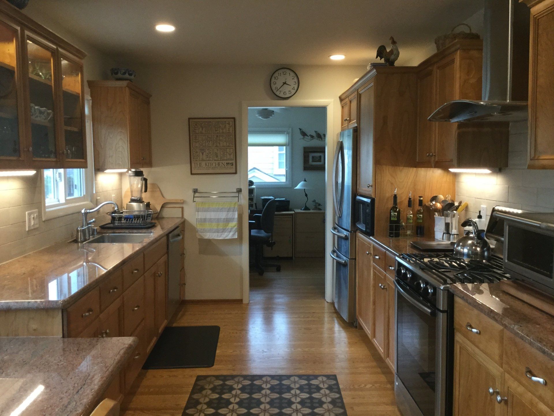 A galley-style kitchen featuring wood cabinets, granite countertops, stainless steel appliances, and a central doorway.