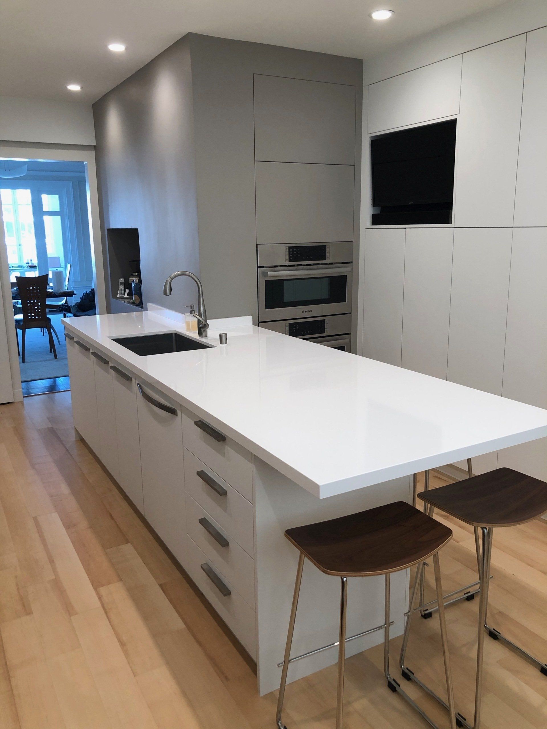 A modern kitchen island with white cabinets, a sink, and two stools on light wood flooring.