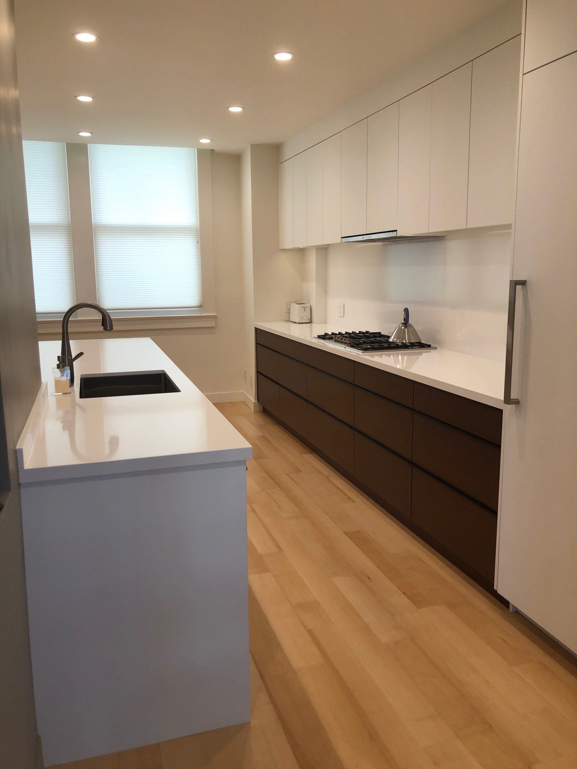 A modern kitchen features a white island with a black sink, dark wood cabinets, white countertops, and light wood flooring.