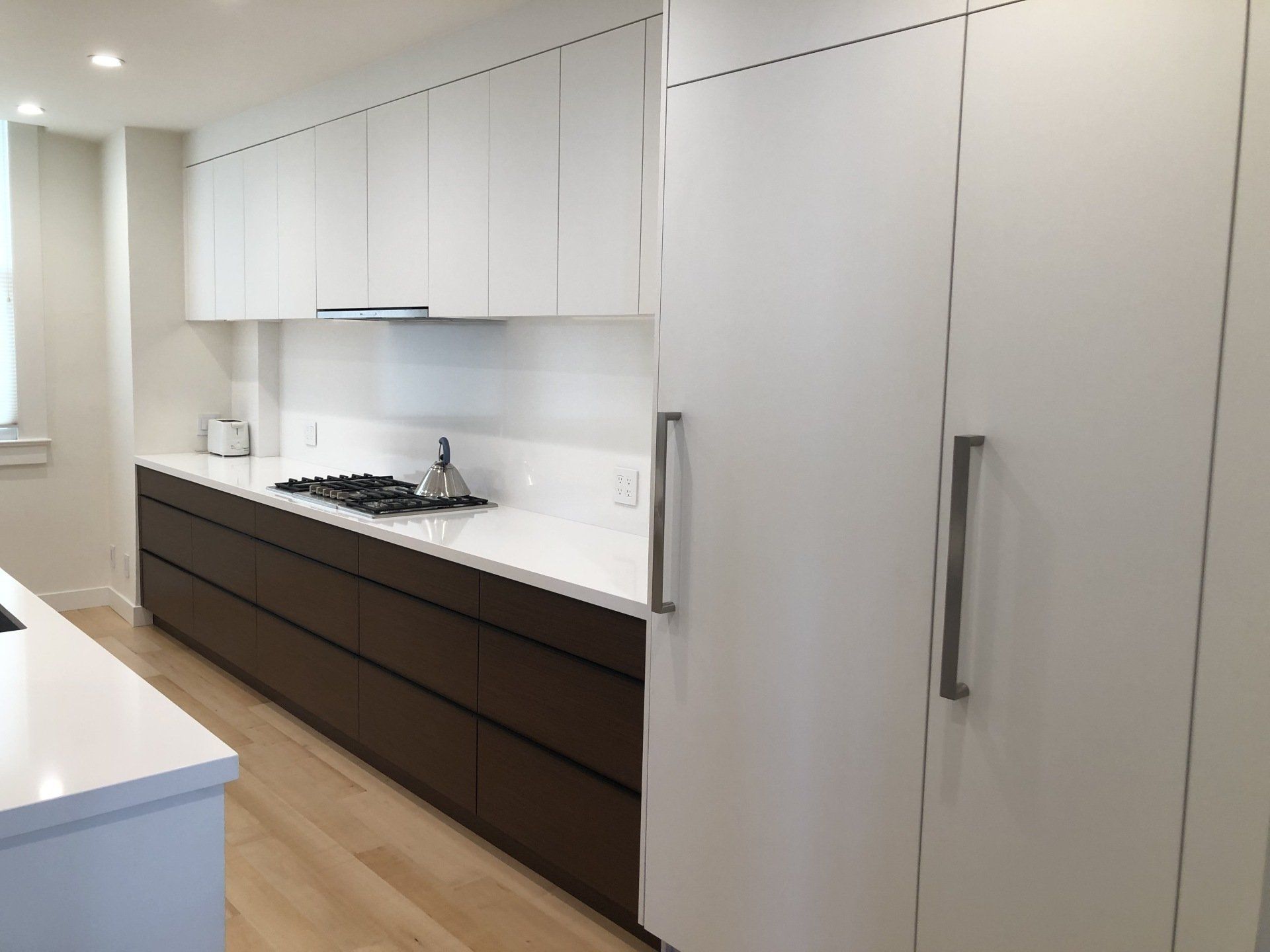 Modern kitchen with white upper cabinets, dark lower cabinets, white countertops, a gas cooktop, and wood floors.