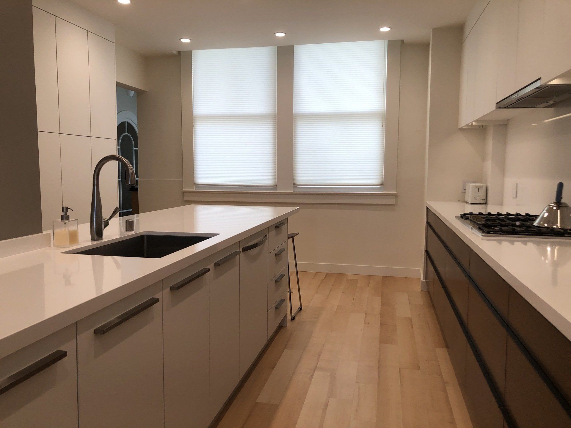 A modern kitchen with a white island, dark lower cabinets, light wood floors, and white countertops.