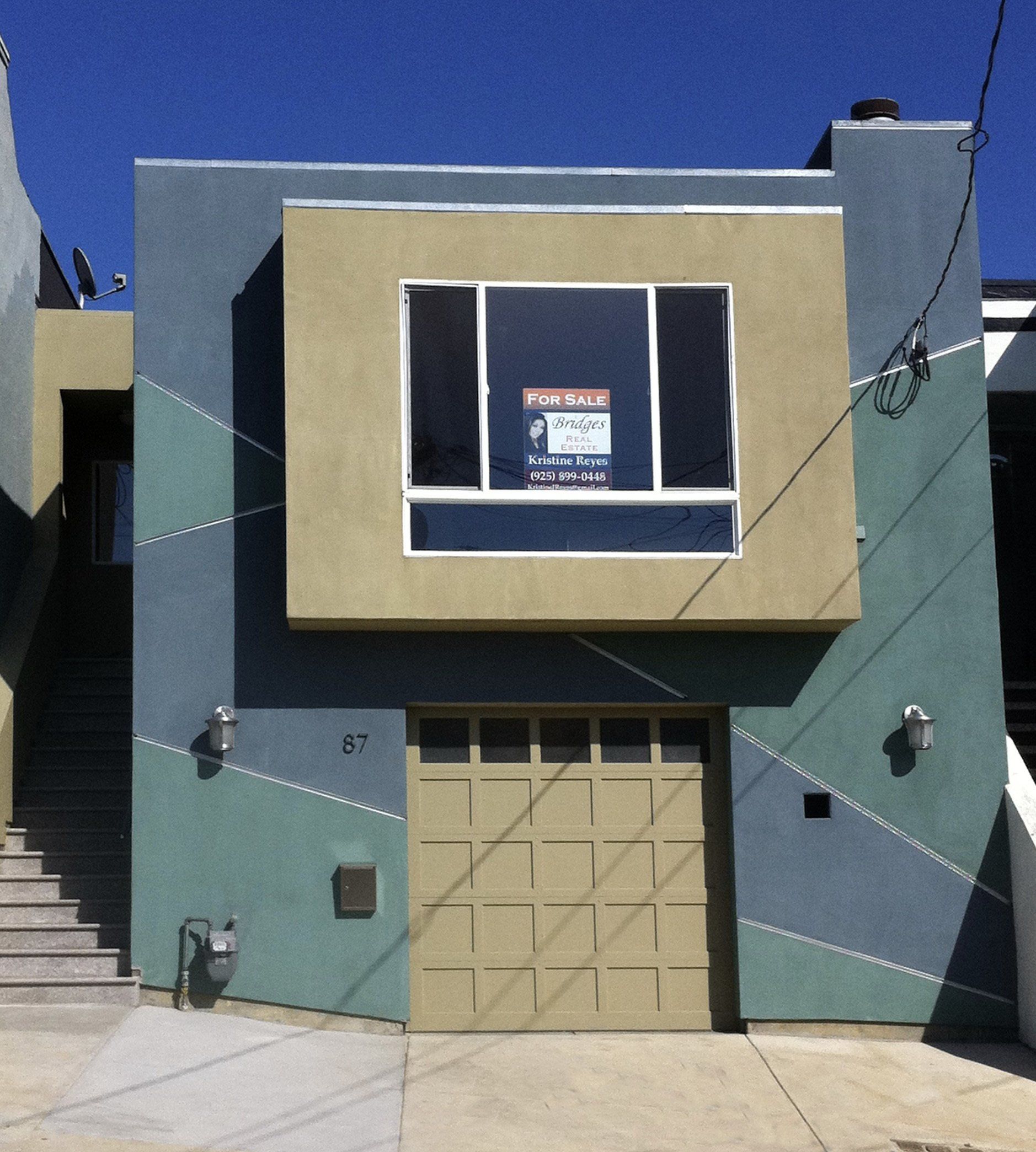 A modern house with a gray exterior, a tan projecting upper window, and a matching tan single-car garage door.