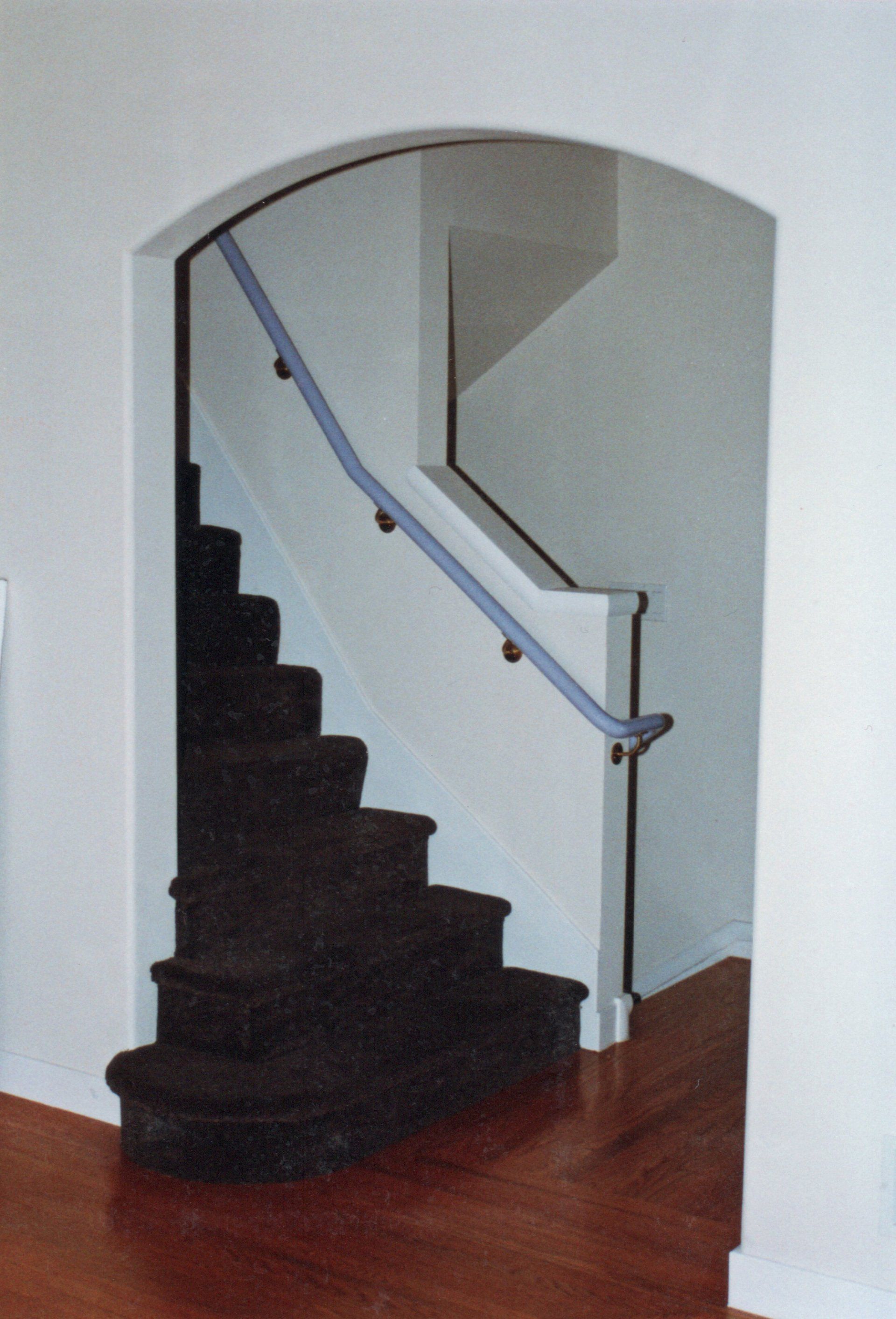 An arched doorway leading to a carpeted staircase with a handrail in a home with hardwood floors.