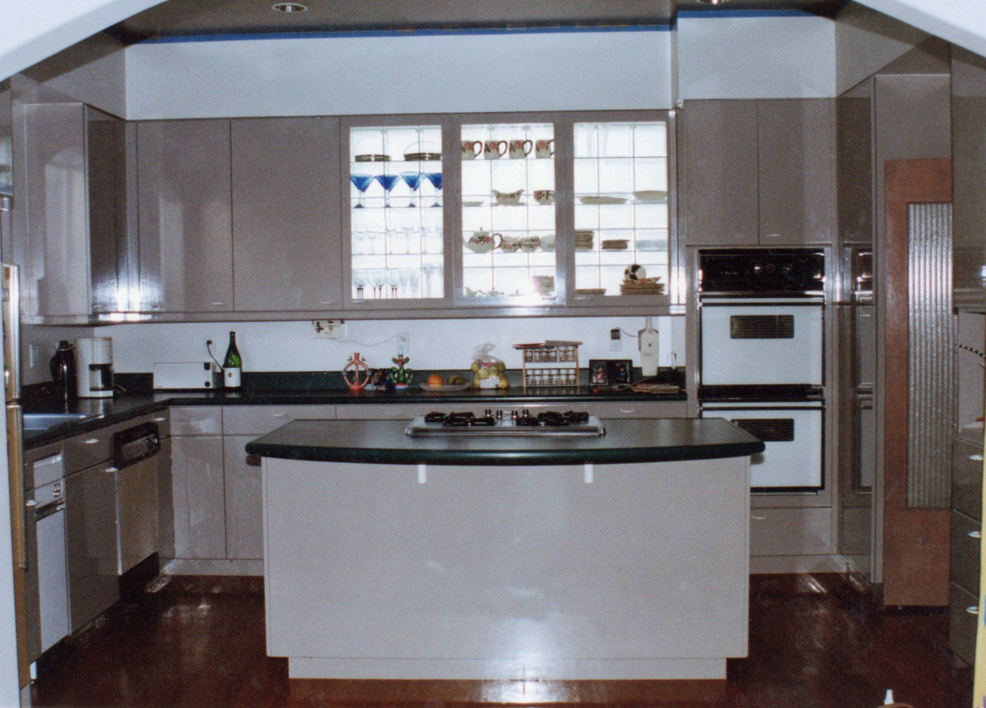 A kitchen featuring light-gray cabinets, a center island with a black countertop, a double oven, and dark hardwood floors.