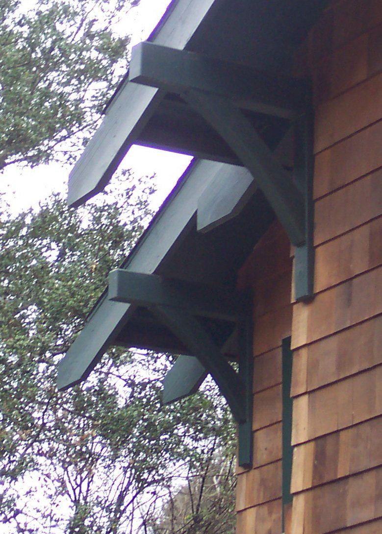 Two dark green wooden brackets supporting a roof overhang on the exterior of a cedar-shingled building.