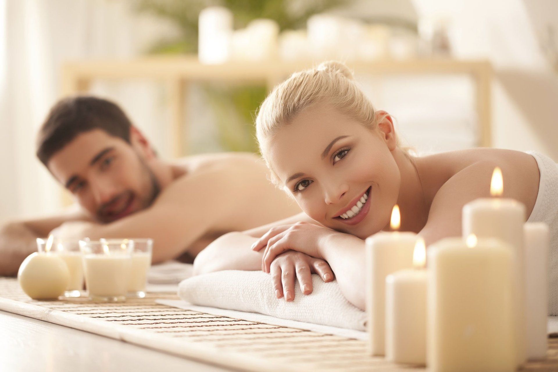 Ein Mann und eine Frau liegen mit Kerzen auf einem Massagetisch.