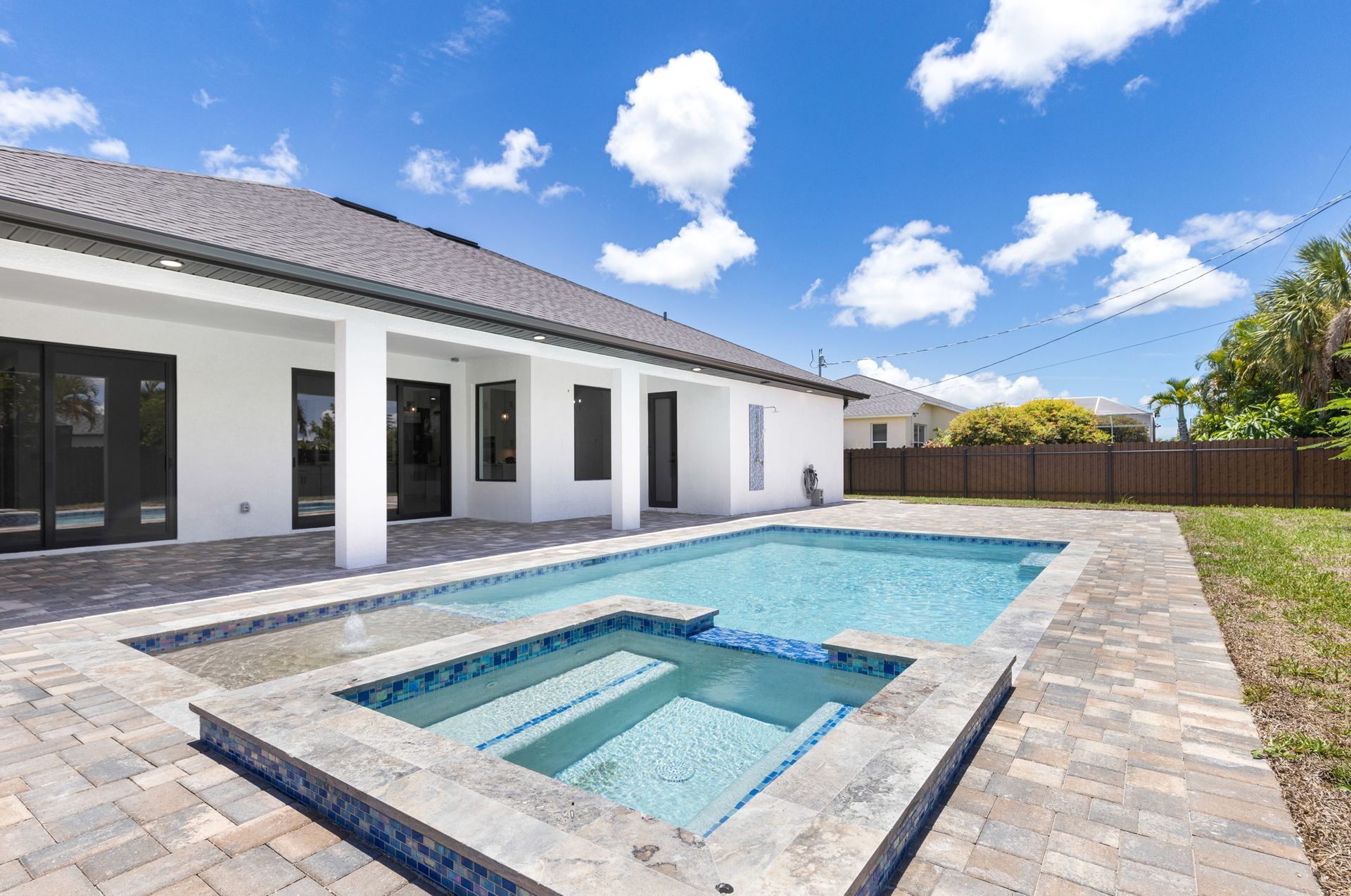Backyard with pool and spa, white house, blue sky.