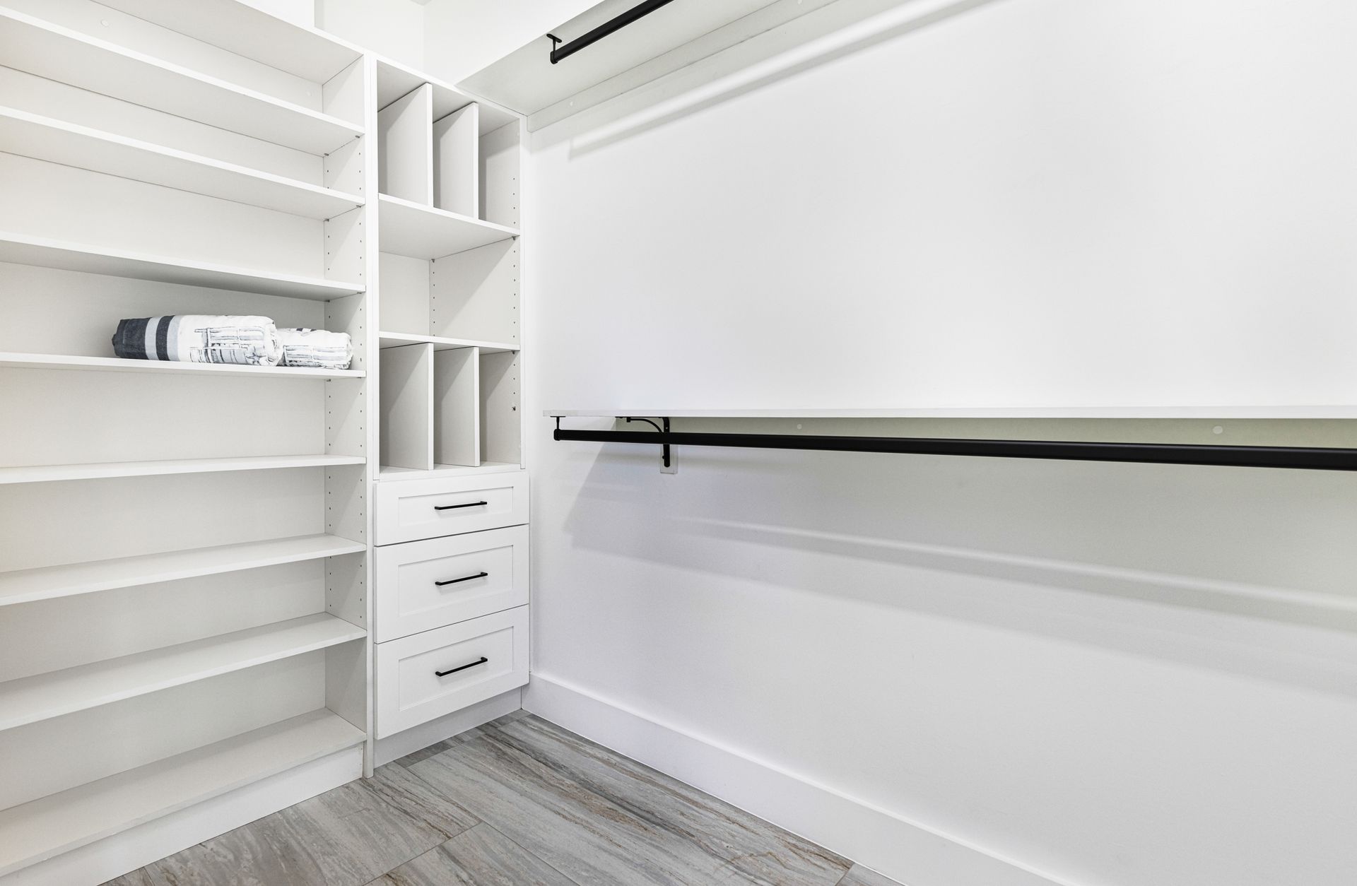 White walk-in closet with shelving, drawers, and a rod for hanging clothes; neutral flooring.