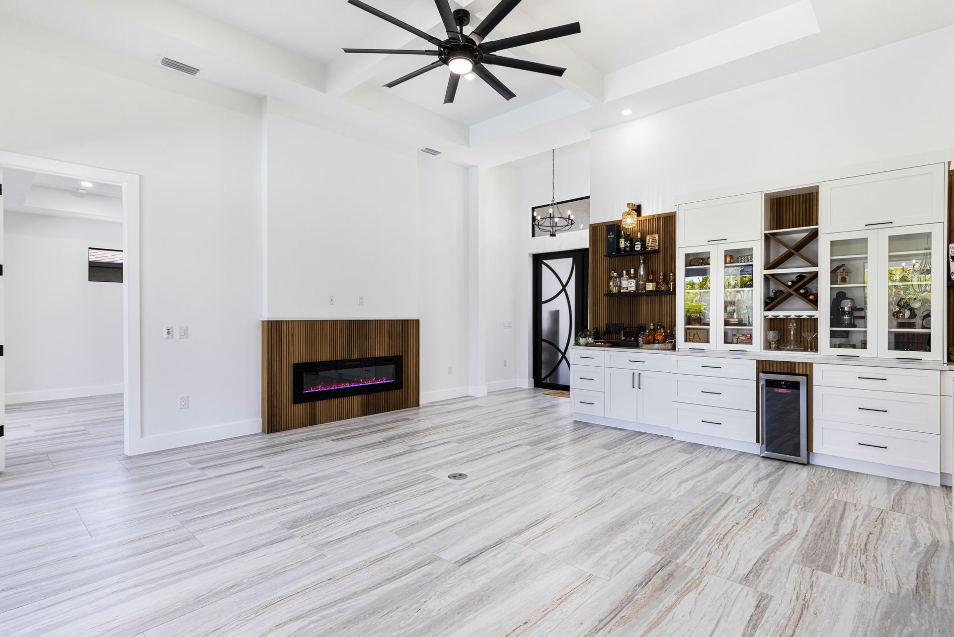 Living room: white walls, wood fireplace, white cabinets, bar area, black ceiling fan, wood-look floors.
