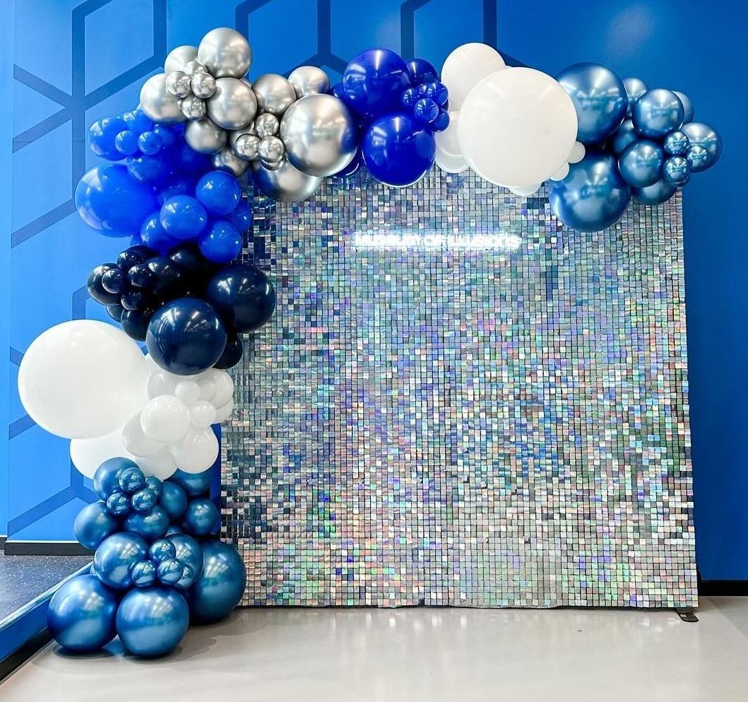A wall covered in blue , white and silver balloons.