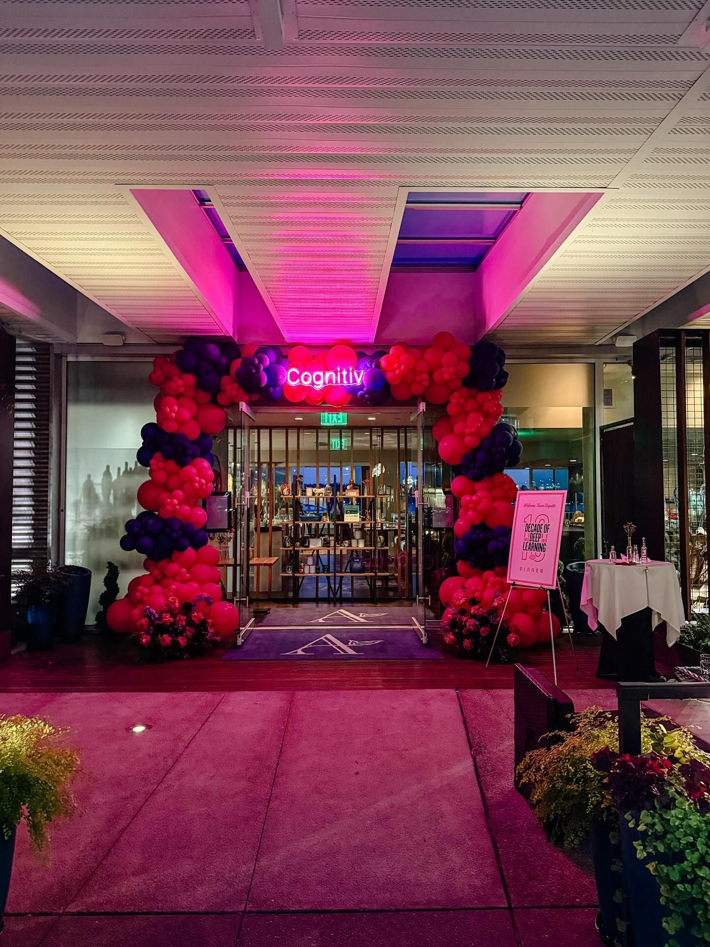 Entrance to a building with pink lighting, balloon arch, and a visible Cognitv sign above the doors