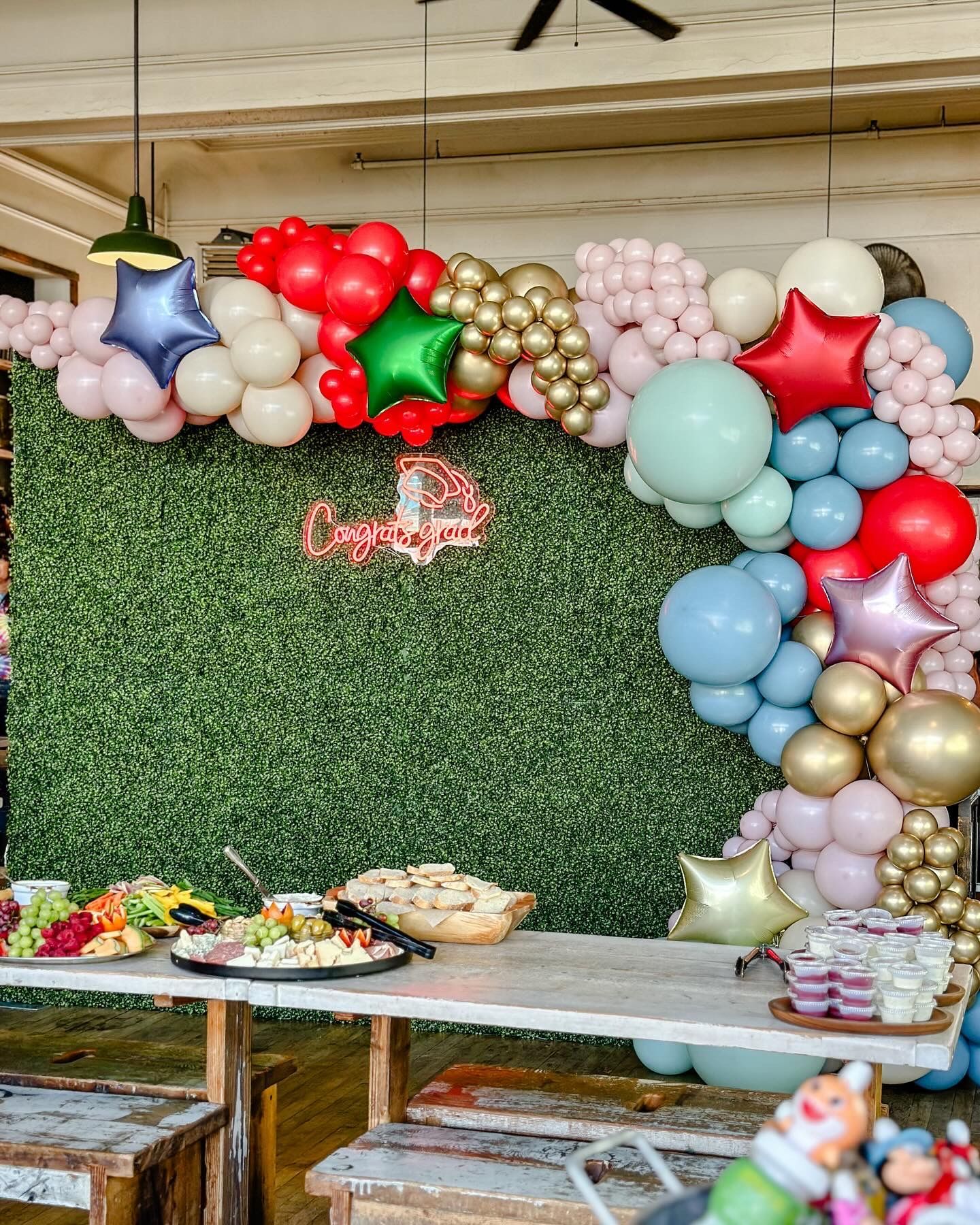A table with food and balloons on it in front of a green wall.
