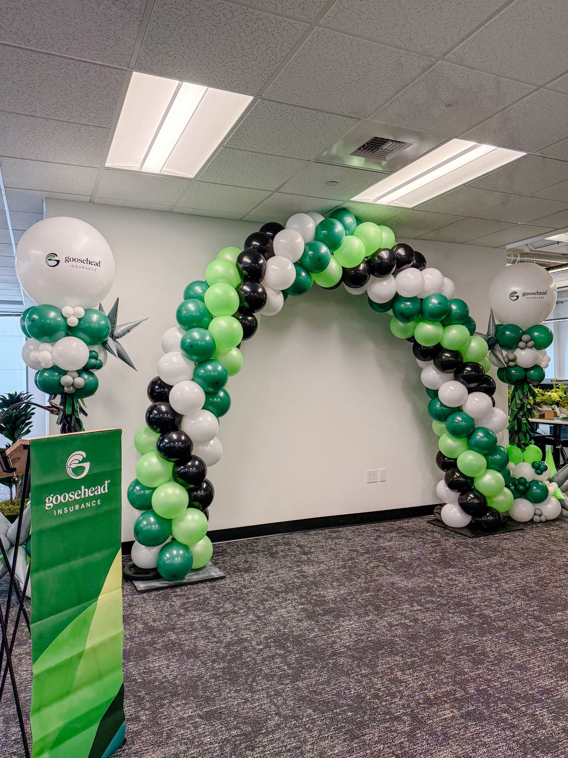 Black, green, and white balloon arch with matching decor in a decorated indoor event space