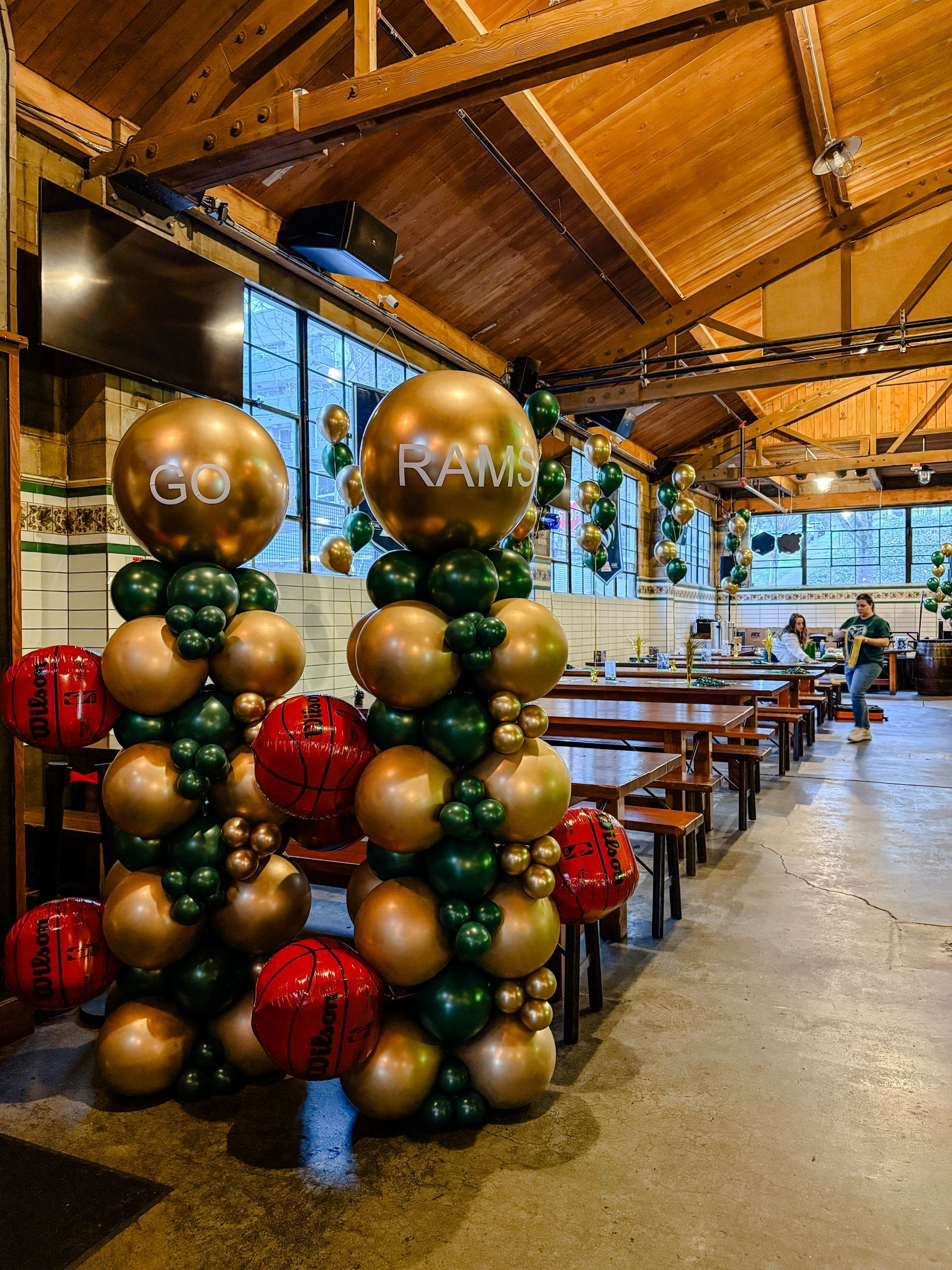 Two balloon columns in a restaurant with gold, green, and red balloons, one with 