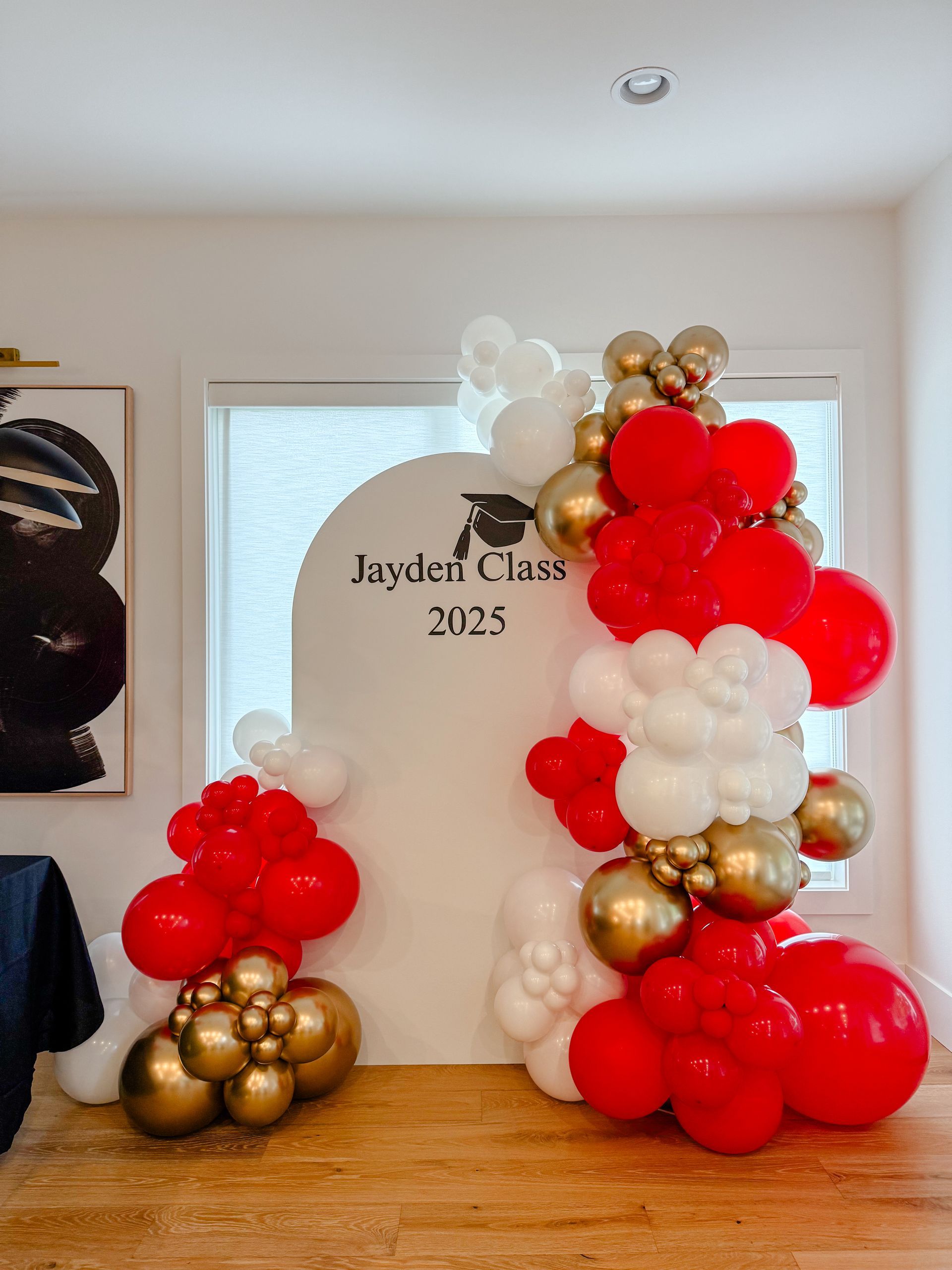 Red, white, and gold balloon arch for graduation with a sign that says