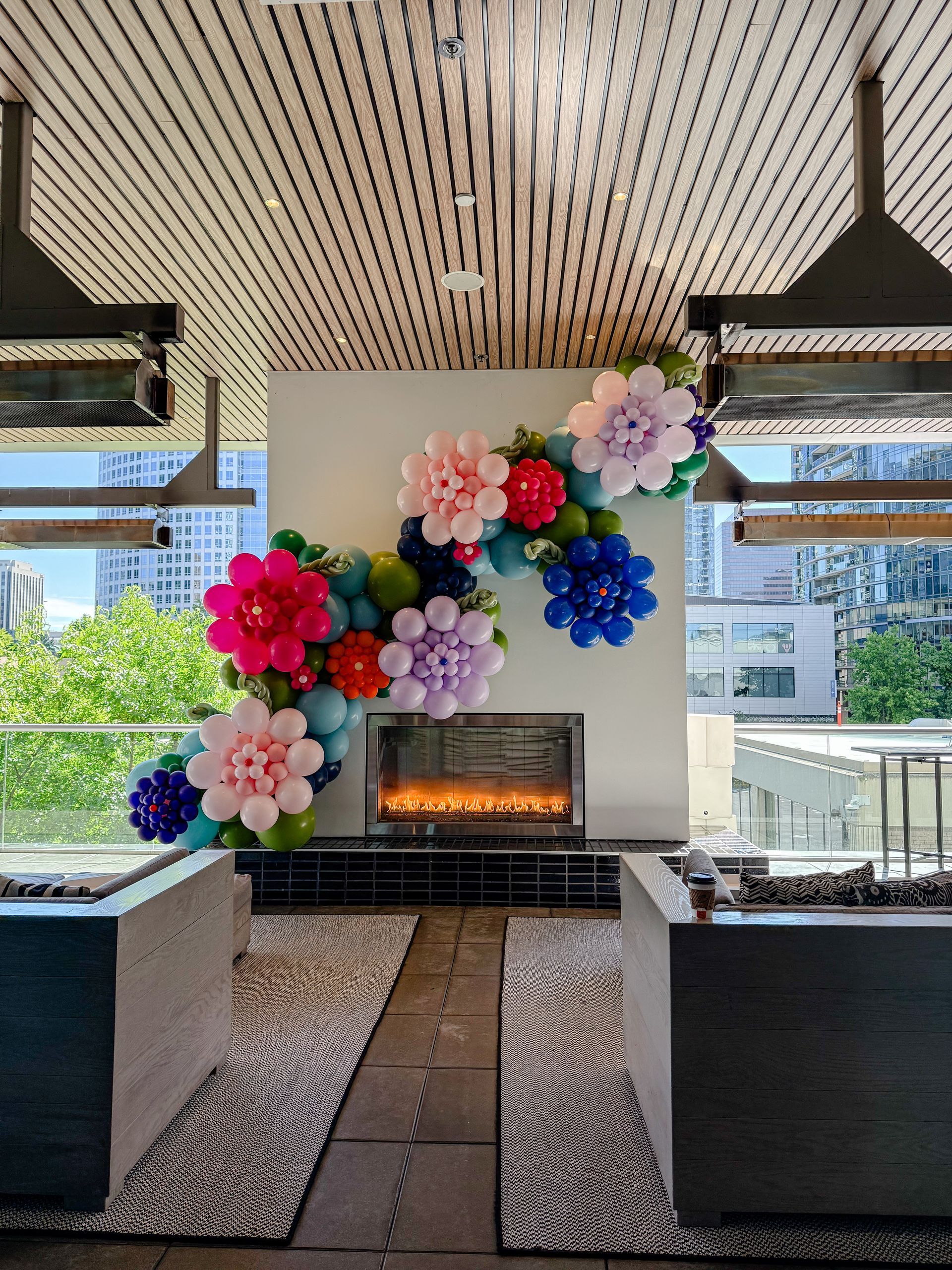 A fireplace features a large, colorful balloon garland shaped like blooming flowers in pink, red, purple, and blue.