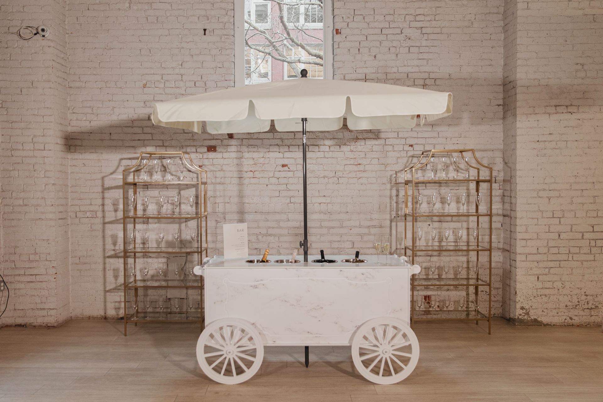 A white cart with a white umbrella is sitting in a room next to a brick wall.