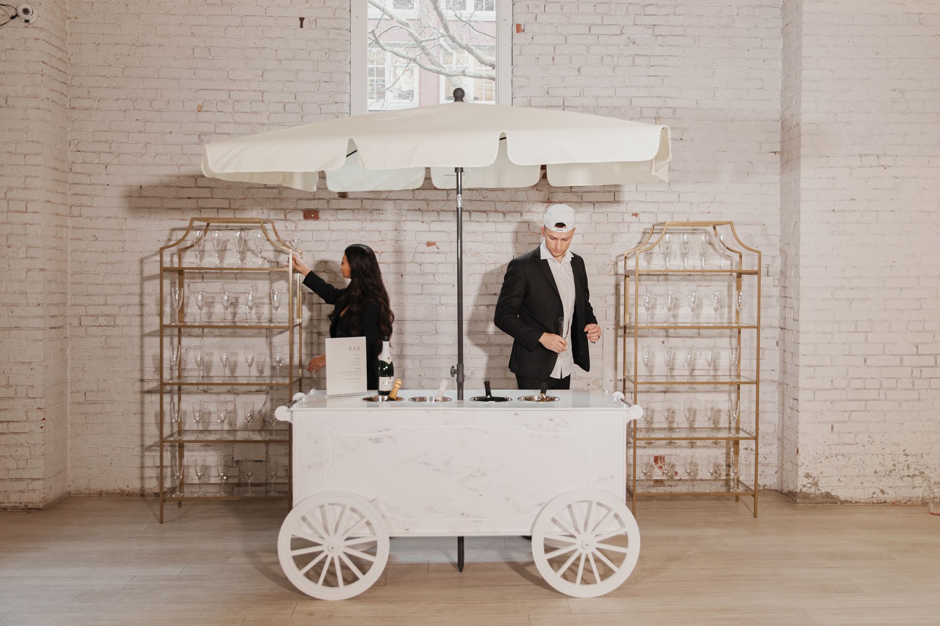 A man and a woman are standing in front of a white cart with a white umbrella.