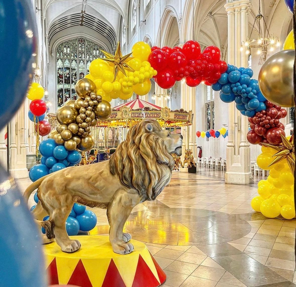 A statue of a lion is surrounded by balloons in a room.