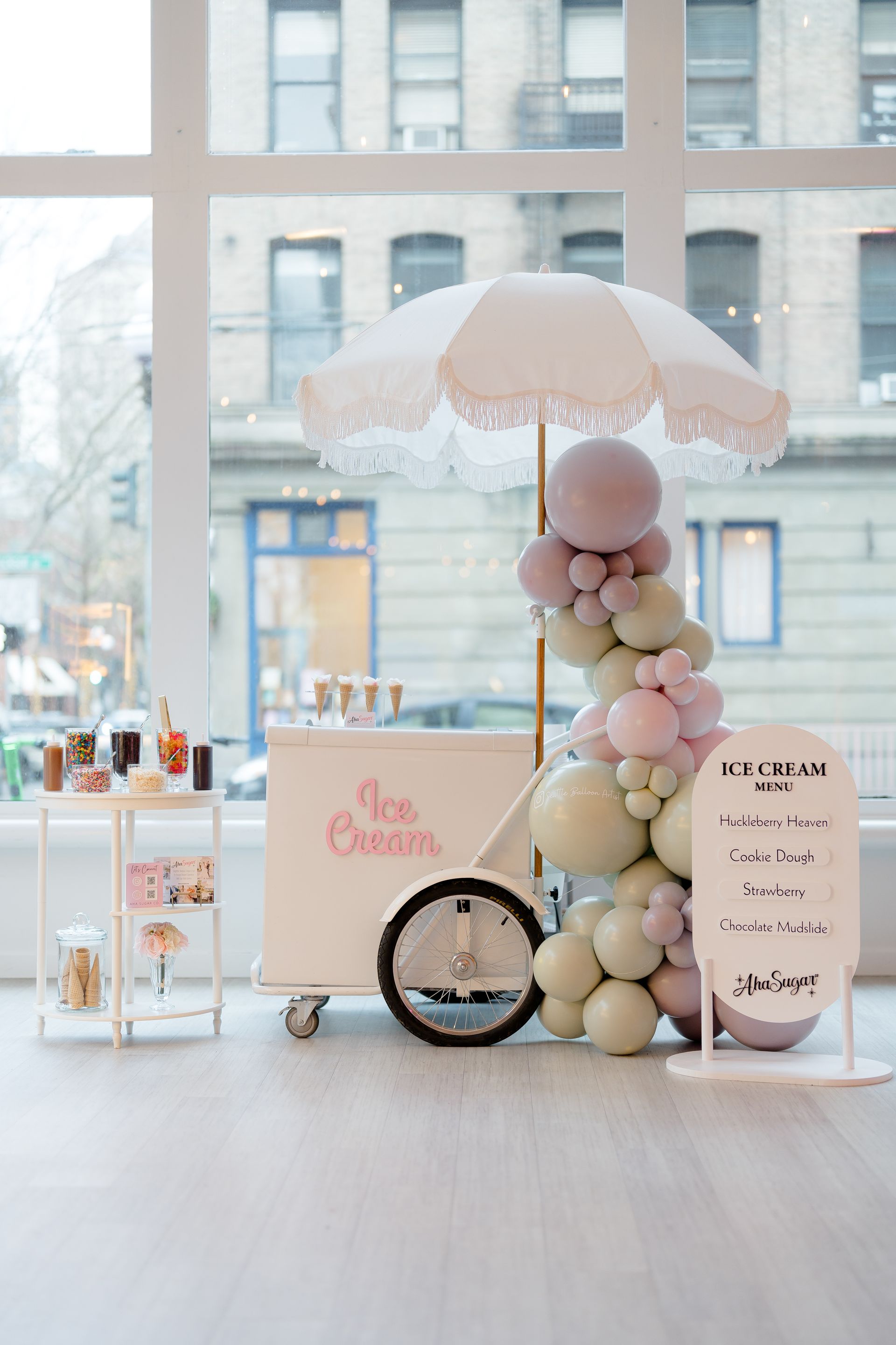 An ice cream cart is decorated with balloons and an umbrella.