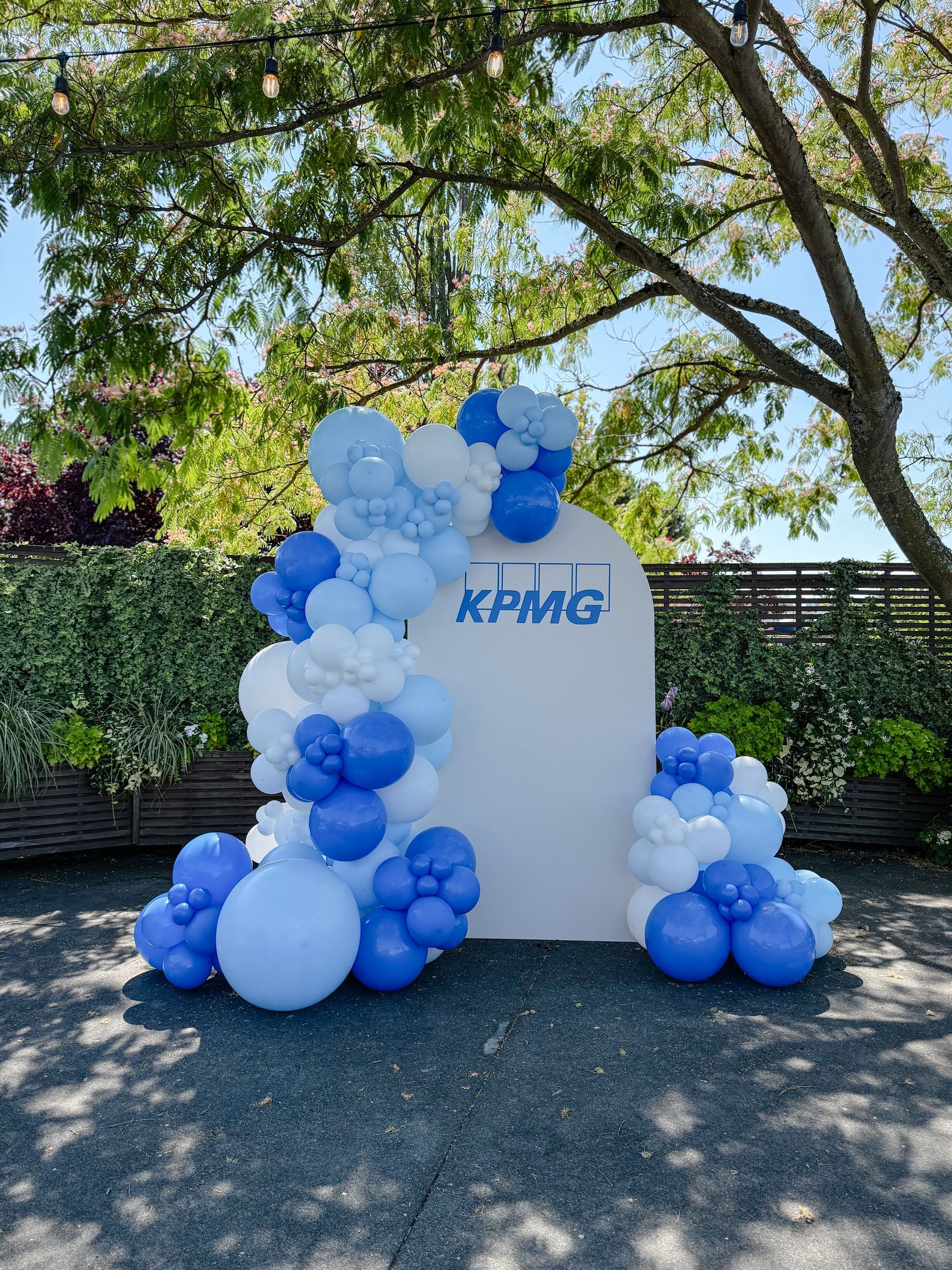 KPMG logo on white backdrop decorated with blue and white balloons outdoors.