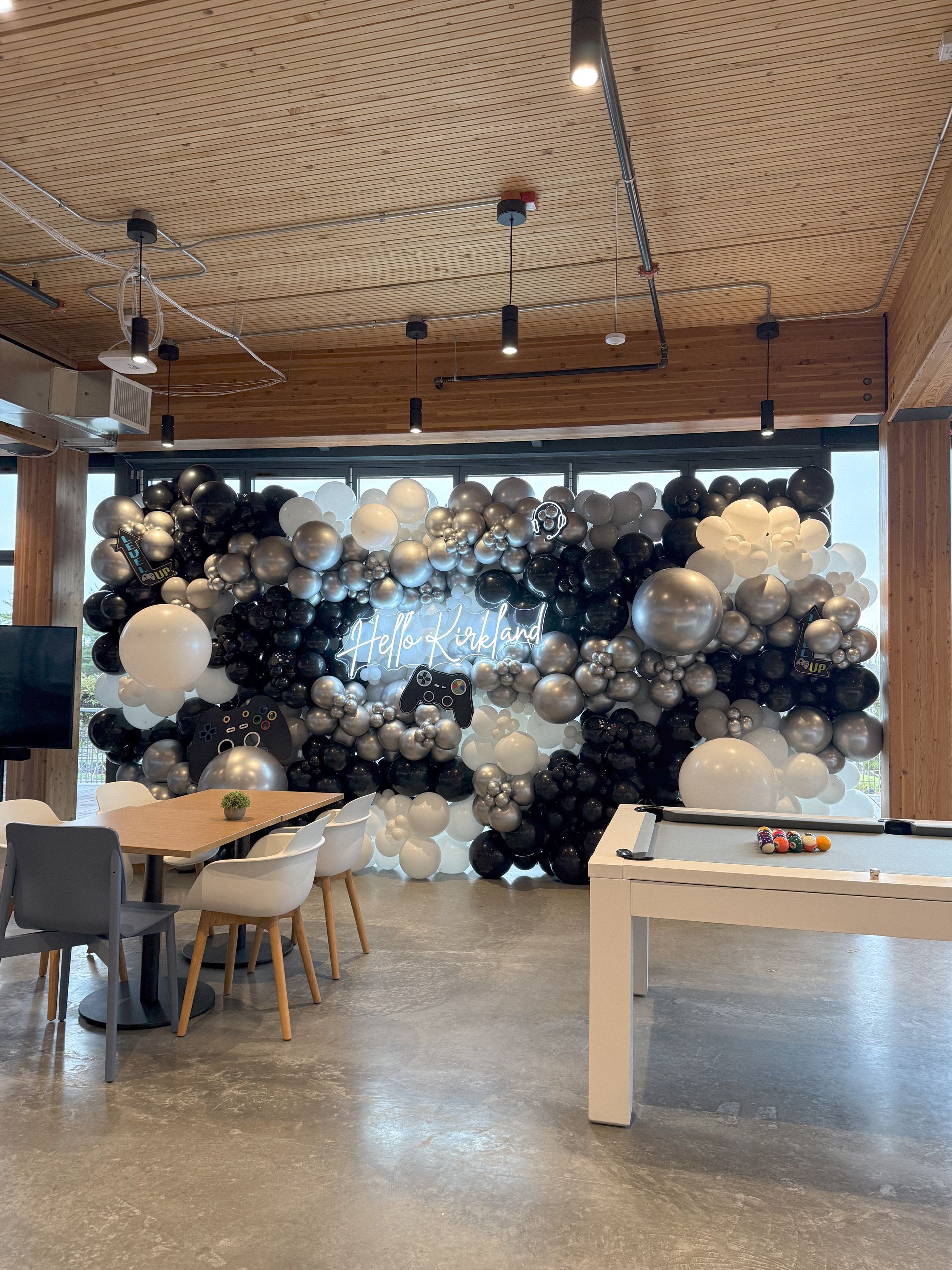 A black, white, and silver balloon arch decoration in a modern room with a pool table and dining area.