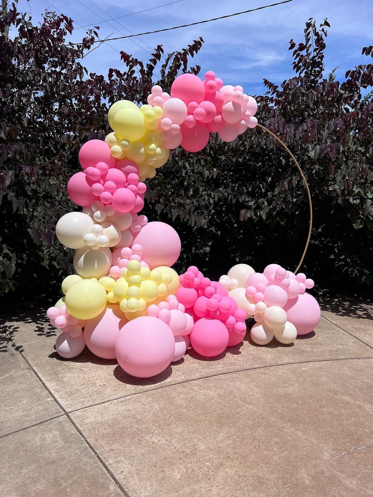 A bunch of pink and yellow balloons are sitting on a sidewalk.